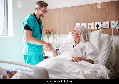 Chirurgo visitando e stringono le mani con femmina matura paziente nel letto di ospedale Foto Stock
