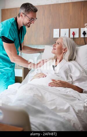 Chirurgo visitando e parlando con femmina matura paziente nel letto di ospedale Foto Stock