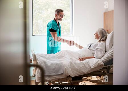 Chirurgo visitando e stringono le mani con femmina matura paziente nel letto di ospedale Foto Stock