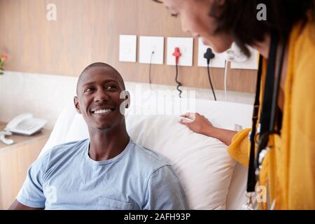 Medico con tavoletta digitale visitando e parlando con il paziente di sesso maschile nel letto di ospedale Foto Stock