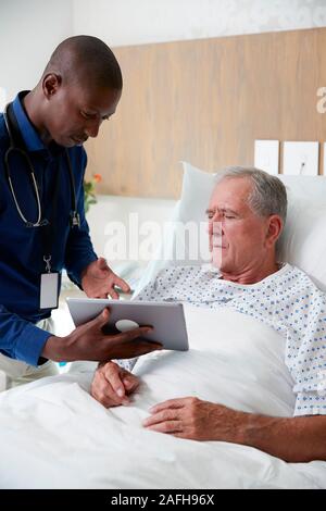 Medico con tavoletta digitale visitando e parlando con i Senior paziente di sesso maschile nel letto di ospedale Foto Stock