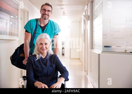 Maschio di spinta ordinata Senior paziente femmina di essere dimesso dall'ospedale in sedia a rotelle Foto Stock