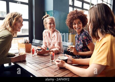 Quattro giovani donne riunione amici siedono al tavolo in un Coffee Shop e parlare Foto Stock