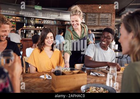 La cameriera che serve un gruppo di giovani amici incontro per un drink e il cibo nel ristorante Foto Stock
