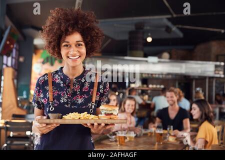 Ritratto di cameriera che serve cibo ai clienti nella trafficata Bar Ristorante Foto Stock