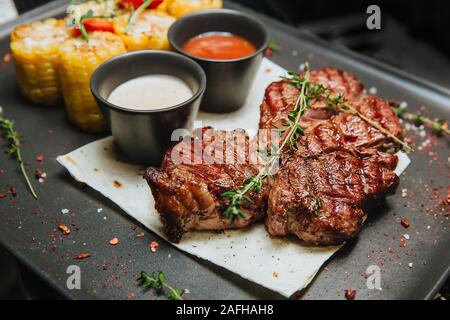 Una succosa carne alla brace bistecca con due salse siede su un quadrato nero piastra . Hot piatti a base di carne. Foto Stock