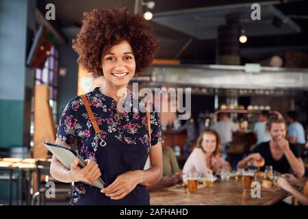 Ritratto di cameriera tenendo premuto Menu che serve nella trafficata Bar Ristorante Foto Stock