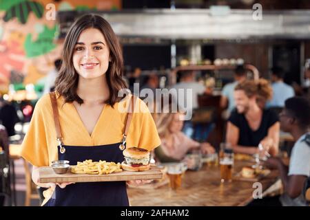 Ritratto di cameriera che serve cibo ai clienti nella trafficata Bar Ristorante Foto Stock