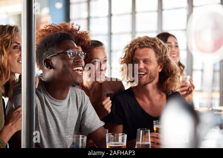 Gruppo di maschio e femmina celebra gli amici mentre si guarda la partita sullo schermo in Sports Bar Foto Stock