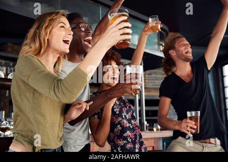 Gruppo di maschio e femmina celebra gli amici mentre si guarda la partita sullo schermo in Sports Bar Foto Stock