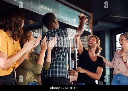 Gruppo di maschio e femmina celebra gli amici mentre si guarda la partita sullo schermo in Sports Bar Foto Stock