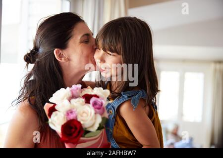 Metà donna adulta baciando la sua figlia, che ha dato un mazzo di fiori per il suo compleanno, close up Foto Stock