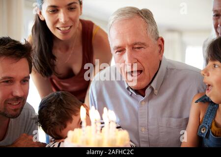 Senior uomo bianco festeggia con la sua famiglia soffiando fuori le candeline sulla torta di compleanno e chiudere fino Foto Stock