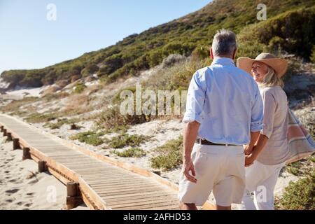 Senior coppia bianco a piedi lungo la passeggiata a mare di legno su una spiaggia Holding Hands, vicino, vista posteriore Foto Stock