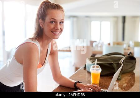 Millenaria donna bianca controllo app fitness sul suo computer portatile dopo la palestra di sorridere alla telecamera, vista laterale Foto Stock