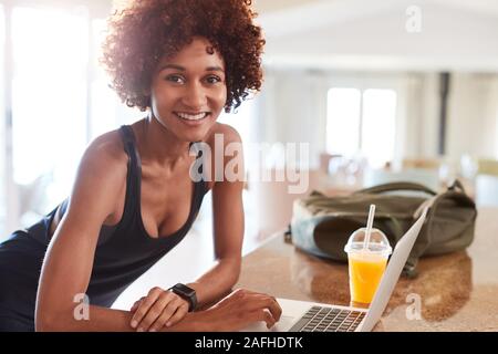 La millenaria americano africano donna verifica i dati di fitness sul computer portatile dopo la palestra di sorridere alla telecamera Foto Stock