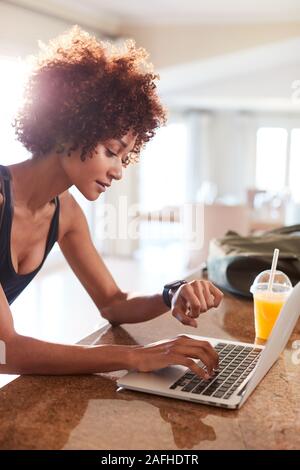 La millenaria americano africano donna controllo app fitness sull'orologio e laptop dopo allenamento, verticale Foto Stock