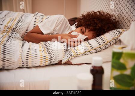 La millenaria americano africano donna giaceva a letto soffia il naso in un tessuto, vista laterale, vicino fino Foto Stock