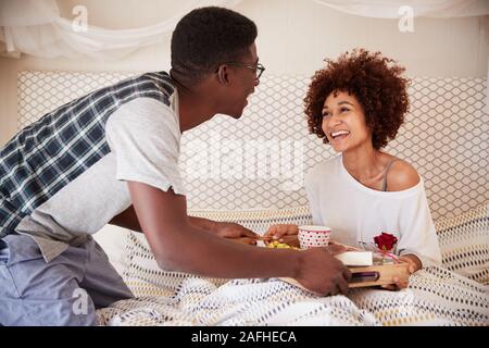 La millenaria americano africano giovane celebrando, l uomo che serve il suo partner la colazione a letto, close up Foto Stock