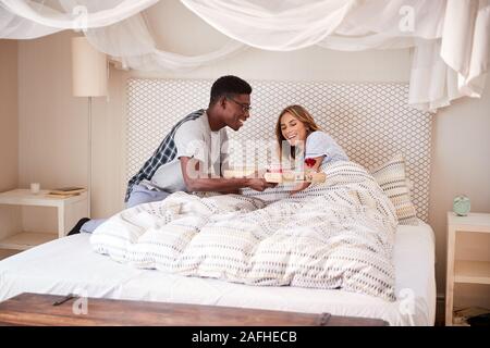 La millenaria razza mista giovane celebrando, l uomo che serve il suo partner la colazione a letto Foto Stock