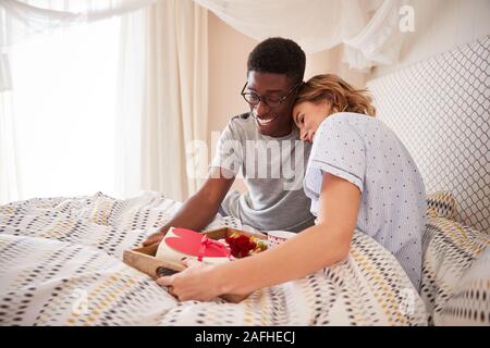 Razza mista giovane abbracciando l'uomo portare il suo partner prima colazione e doni a letto, close up Foto Stock