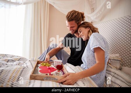 Bianco millenario giovane abbracciando, dopo l'uomo serve la prima colazione e i doni in letto, close up Foto Stock