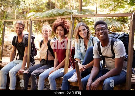 Cinque giovani amici adulti su una escursione seduti insieme sorridente alla fotocamera durante una pausa, close up Foto Stock