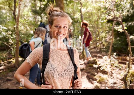 Ritratto di millenaria donna bianca con legato i capelli escursionismo in una foresta con i suoi amici, close up Foto Stock