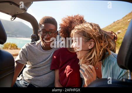 Tre giovani felici amici adulti seduti in una vettura aperta dalla costa, vicino alla cintura fino Foto Stock