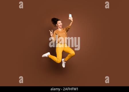 Lunghezza piena dimensione corpo foto di allegro dolce abbastanza trendy ed elegante affascinante ragazza positiva che mostra v-firmare la registrazione di un video tenendo selfie jumping Foto Stock