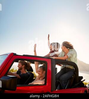 Cinque giovani amici adulti in un viaggio su strada guidando in una sommità aperta jeep in riva al mare Foto Stock