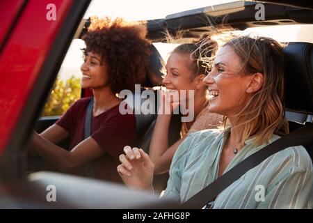 Tre femmina millenario amici in un viaggio su strada la guida insieme in una jeep aperta, chiudere fino Foto Stock