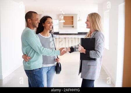 Agente immobiliare femmina stringono le mani con coppia interessati all'acquisto di casa Foto Stock
