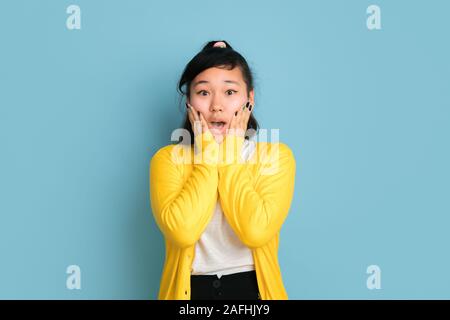 Asian adolescente il ritratto isolato su blu di sfondo per studio. Bellissima femmina modello bruna con capelli lunghi in stile casual. Concetto di emozioni umane, l'espressione del viso, vendite, annuncio. Guarda scioccato. Foto Stock