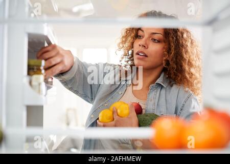 Vista dall'interno del frigorifero come donna apre la porta e pacchi cibo su ripiani Foto Stock