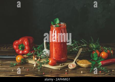 In casa naturale DIY conserve di pomodoro calda chutney di salsa al peperoncino o adjika nel vasetto di vetro in piedi sul tavolo di legno con pomodorini, sale, pepe, h Foto Stock