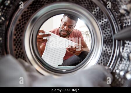 Vista dall'interno della macchina di lavaggio come l uomo tiene fuori vestiti del bambino Foto Stock