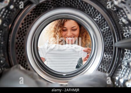 Vista dall'interno della macchina di lavaggio come donna prende vestiti del bambino Foto Stock