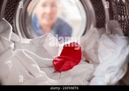 Donna che guarda all'interno della macchina di lavaggio con calza rossa mescolato con il bianco Servizio Lavanderia Foto Stock