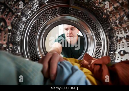 Vista dall'interno della macchina di lavaggio come giovane uomo fa servizio lavanderia Foto Stock