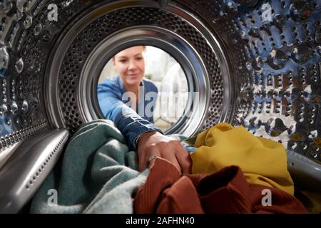 Vista dall'interno della macchina di lavaggio come giovane donna fa servizio lavanderia Foto Stock