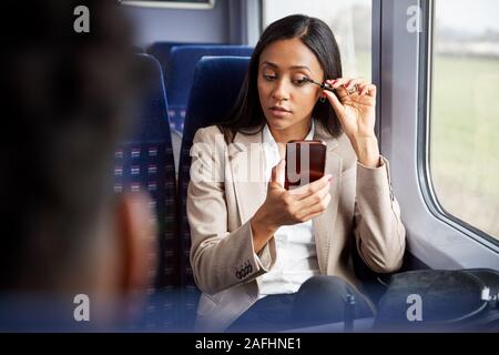 Imprenditrice seduta in treno Pendolari mettendo su Make Up Foto Stock