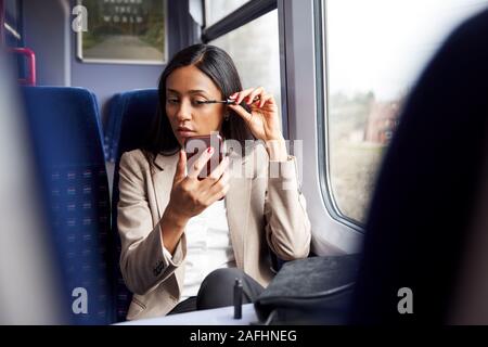 Imprenditrice seduta in treno Pendolari mettendo su Make Up Foto Stock