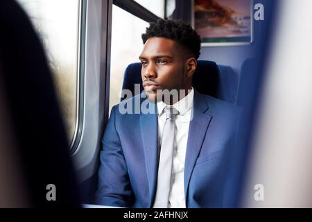 Imprenditore seduto in treno il pendolarismo a lavorare guardando fuori della finestra Foto Stock