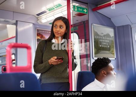 Femmina in piedi passeggero da porte In treno usando il telefono cellulare Foto Stock