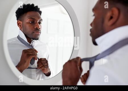 Imprenditore a casa la legatura cravatta in Mirror prima di lasciare per il lavoro Foto Stock