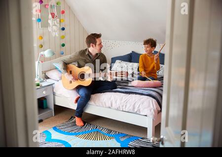 Unico Padre suonare la chitarra con il figlio che tamburi sul cuscino in camera da letto Foto Stock