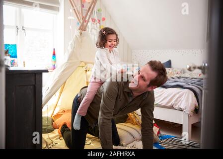 Figlia di equitazione padri sul retro come essi svolgono In Den In camera da letto a casa Foto Stock