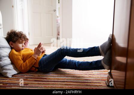 Ragazzo disteso sul pavimento della camera da letto di passare troppo tempo utilizzando il telefono cellulare Foto Stock