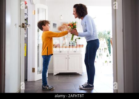 Amare il figlio dando madre mazzo di fiori per celebrare la festa della mamma a casa Foto Stock